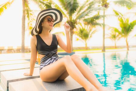 Portrait beautiful young asian woman relax around outdoor swimming pool in hotel resort with palm tree at sunset or sunrise for leisure vacationの写真素材
