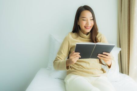 Young asian woman with coffee cup and read book on bed in bedroom interior
