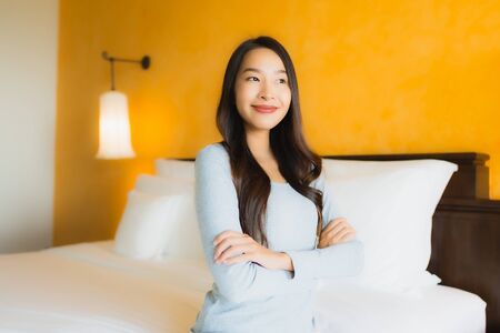 Portrait beautiful young asian woman happy smile relax on bed in bedroom interiorの写真素材