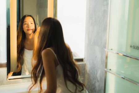 Portrait beautiful young asian woman make up with cosmetic powder and lipstick on her face facial in bathroom interiorの写真素材
