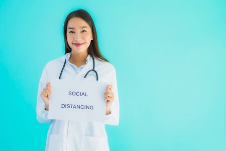 Portrait beautiful young asian doctor woman with sign paper with social distancing word for protect from covid19 or coronavirusの写真素材