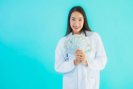 Portrait beautiful young asian doctor woman with a lot of cash and money on blue isolated background