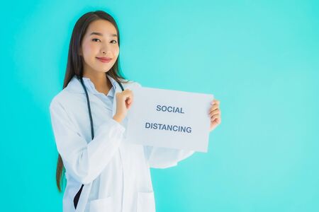 Portrait beautiful young asian doctor woman with sign paper with social distancing word for protect from covid19 or coronavirusの写真素材