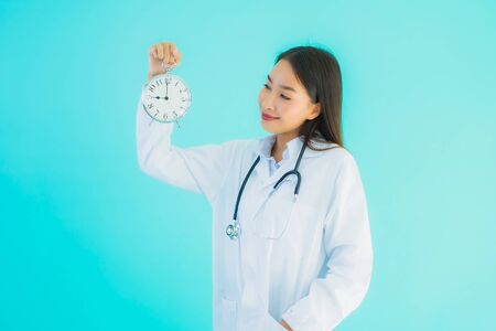 Portrait beautiful young asian doctor woman with clock or alarm on blue isolated backgroundの写真素材