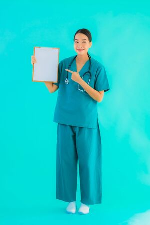 Portrait beautiful young asian doctor woman with empty paper board for copy space on blue isolated background - Healthcare in hospital and clinic conceptの写真素材
