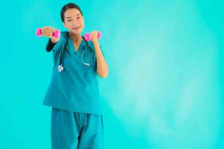 Portrait beautiful young asian doctor woman exercise with dumbbell on blue isolated backgroundの写真素材