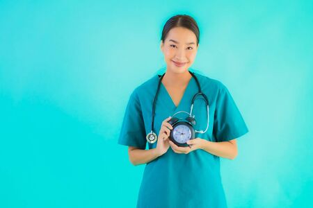 Portriat beautiful young asian doctor woman show clock or alarm on blue isolated backgroundの写真素材