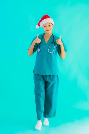 Portrait beautiful young asian doctor woman wear christmas hat with smile happy on blue isolated backgroundの写真素材