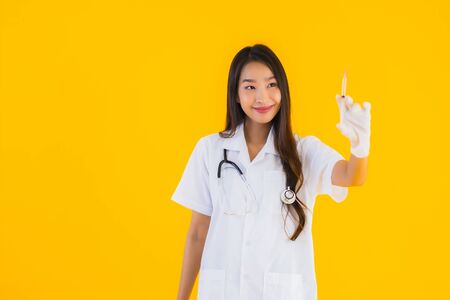 Portrait beautiful young asian doctor woman wear glove use syringe on yellow isolated backgroundの写真素材