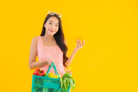 Portrait beautiful young asian woman with grocery in basket shopping from supermarket on yellow isolated backgroundの写真素材