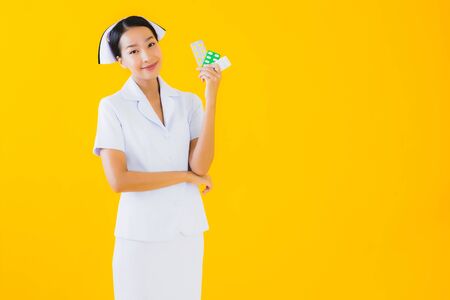 Portrait beautiful young asian woman thai nurse with pill or drug on yellow isolated backgroundの写真素材