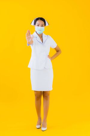Portrait beautiful young asian woman thai nurse wear mask for protect covid19 or coronavirus and show alcohol gel on yellow isolated backgroundの写真素材