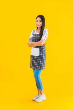Portrait beautiful young asian woman wear apron with smile happy on yellow isolated backgroundの写真素材