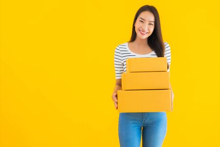 Portrait beautiful young asian woman with parcel box ready for shipping on yellow isolated...