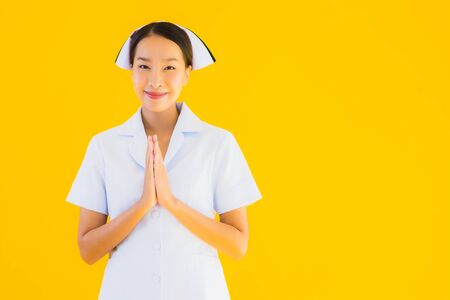 Portrait beautiful young asian thai nurse sawasdee or say hello in Thai on yellow isolated backgroundの写真素材