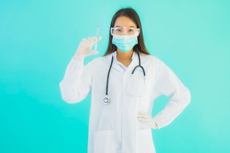 Portrait beautiful young asian doctor woman with vaccine syringe and drung or medicine bottle for use in hospital or clinic on blue isolated backgroundの写真素材