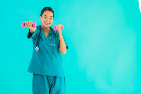 Portrait beautiful young asian doctor woman exercise with dumbbell on blue isolated backgroundの写真素材
