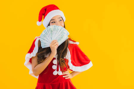 Portrait beautiful young asian woman wear christmas clothes and hat with cash and money on yellow...