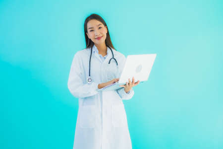 Portrait beautiful young asian doctor woman with laptop for use in clinic or hospital on blue isolated backgroundの写真素材