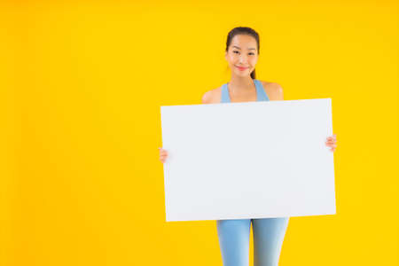Portrait beautiful young asian woman wear sportwear show empty white billboard on yellow isolated backgroundの写真素材