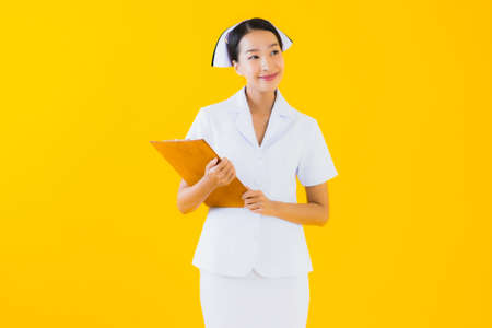 Portrait beautiful young asian woman thai nurse show empty white board and work at clinic or hospital on yellow isolated backgroundの写真素材