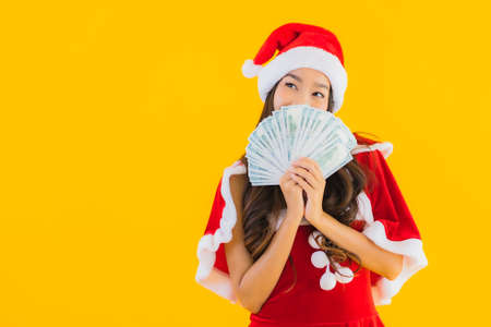 Portrait beautiful young asian woman wear christmas clothes and hat with cash and money on yellow isolated backgroundの写真素材