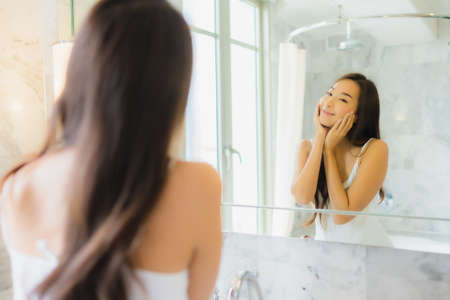 Portrait of beautiful young asian woman watching herself at the mirrorの写真素材