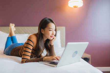 Portrait beautiful young asian woman use laptop computer on bed with credit card in bedroom interior