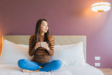 Portrait beautiful young asian woman with coffee cup on bed in bedroom interiorの写真素材