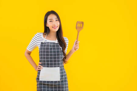 Portrait beautiful young asian woman  wear apron with black pan and Spatula on yellow isolated backgroundの写真素材