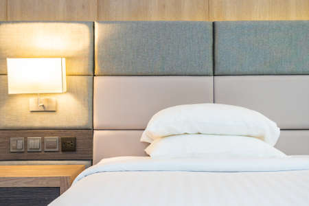 White comfortable pillow and blanket on bed with light lamp decoration interior of bedroomの写真素材