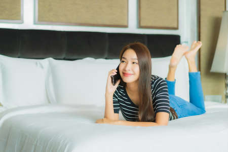 Portrait beautiful young asian woman use smart mobile phone on bed in bedroom interiorの写真素材