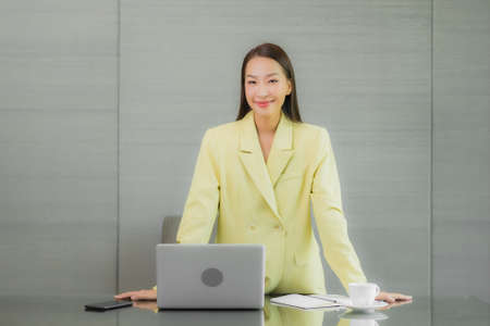 Portrait beautiful young asian woman use computer laptop with smart mobile phone on working table at...