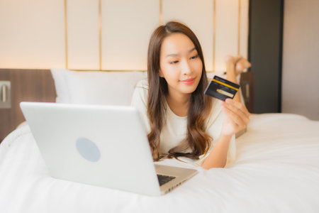 Portrait beautiful young asian woman use laptop on bed in bedroom interiorの写真素材