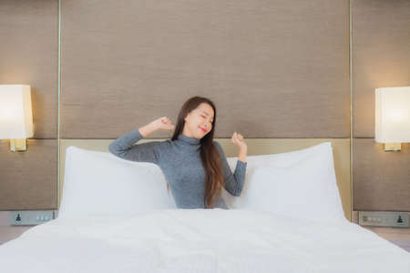 Portrait beautiful young asian woman use smart mobile phone on bed in bedroom interior
