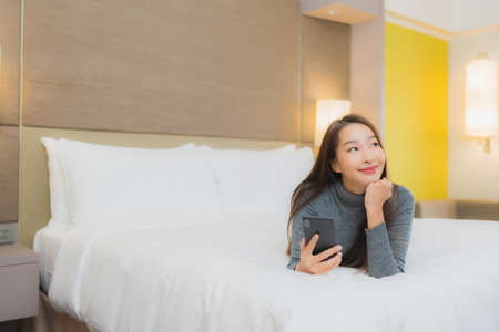 Portrait beautiful young asian woman use smart mobile phone on bed in bedroom interiorの写真素材