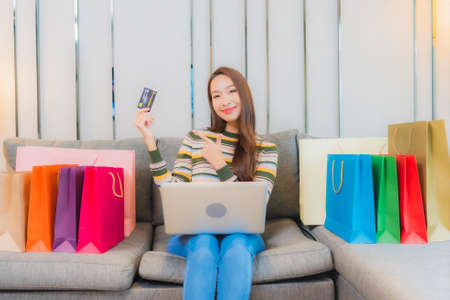 Portrait young asian woman using laptop computer with smart mobile phone and credit card for online shopping in living roomの写真素材