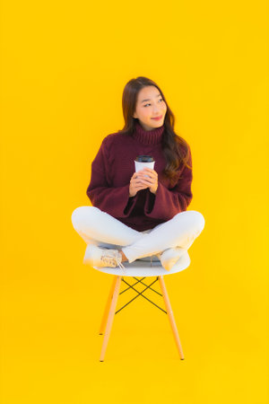Portrait beautiful young asian woman sit on chair with yellow isolated backgroundの写真素材