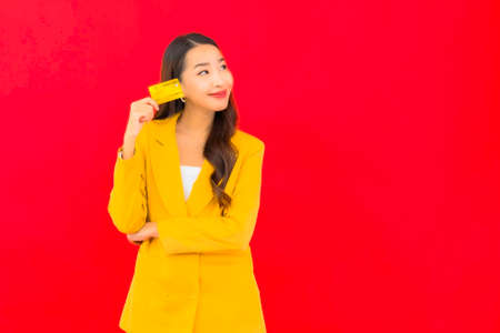 Portrait beautiful young asian woman use mobile with credit card on red background
