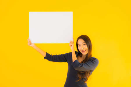 Portrait beautiful young asian woman with empty and blank billboard card banner on yellow isolated...
