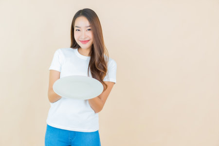 Portrait beautiful young asian woman with empty dish plate with cream color backgroundの写真素材