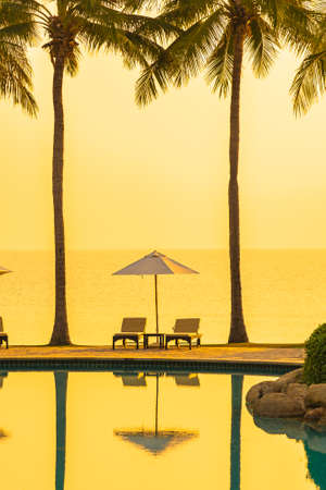 Umbrella and chair around outdoor swimming pool with sea beach ocean at sunset or sunrise timeの写真素材