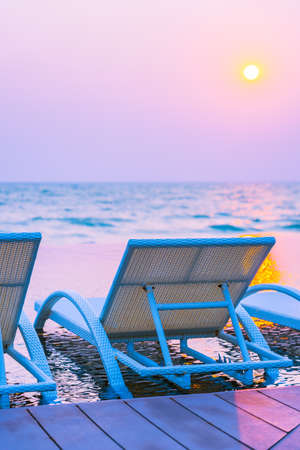 Empty chair around outdoor swimming pool in hotel resort at sunset or sunrise time for leisure...