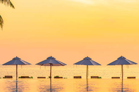 Umbrella deck chair around swimming pool in hotel resort with sea ocean beach and coconut palm tree at sunset or sunrise timeの写真素材