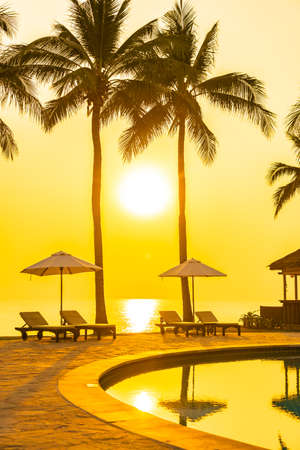 Umbrella and chair around outdoor swimming pool with sea beach ocean at sunset or sunrise timeの写真素材