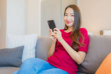 Portrait beautiful young asian woman use smart mobile phone on sofa in living area at bedroom...