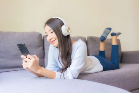 Portrait beautiful young asian woman use smart mobile phone headphone for listen music in living roomの写真素材