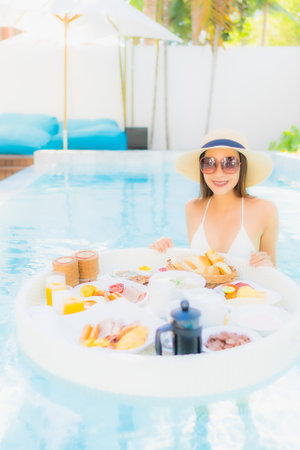 Portrait beautiful young asian woman happy smile with floating breakfast in tray on swimming poolの写真素材