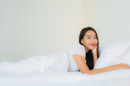 Portrait beautiful young asian woman relax happy smile on bed with white pillow blanket interior of bedroomの写真素材