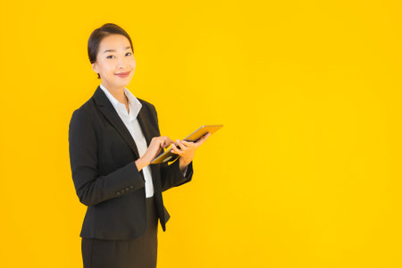 Portrait beautiful young asian woman happy smile with smart tablets device on yellow isolated backgroundの写真素材